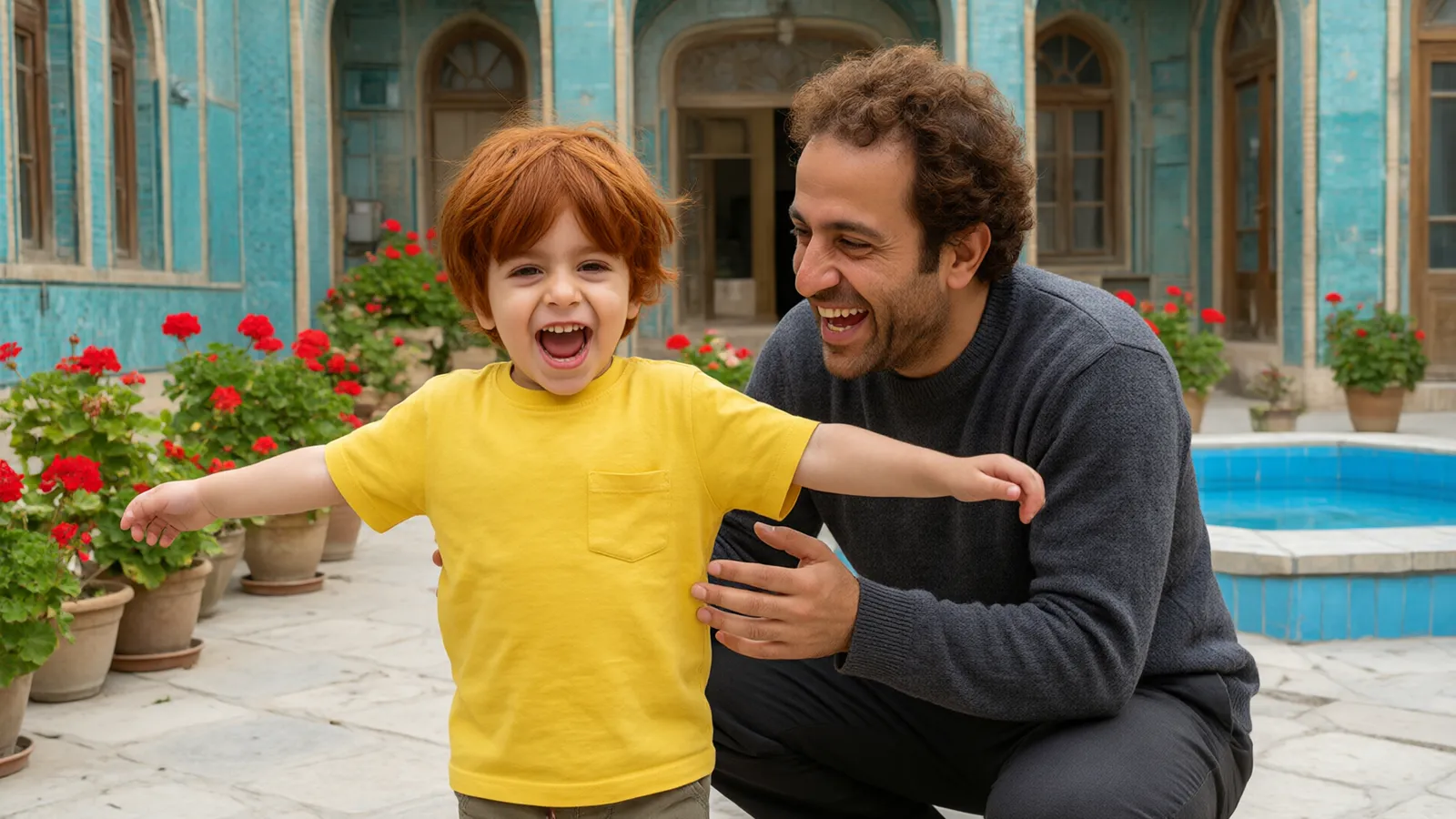پسر سهساله با تیشرت زرد در حیاط کاشی فیروزهای با شادی میچرخد و پدر با پلیور خاکستری میخندد